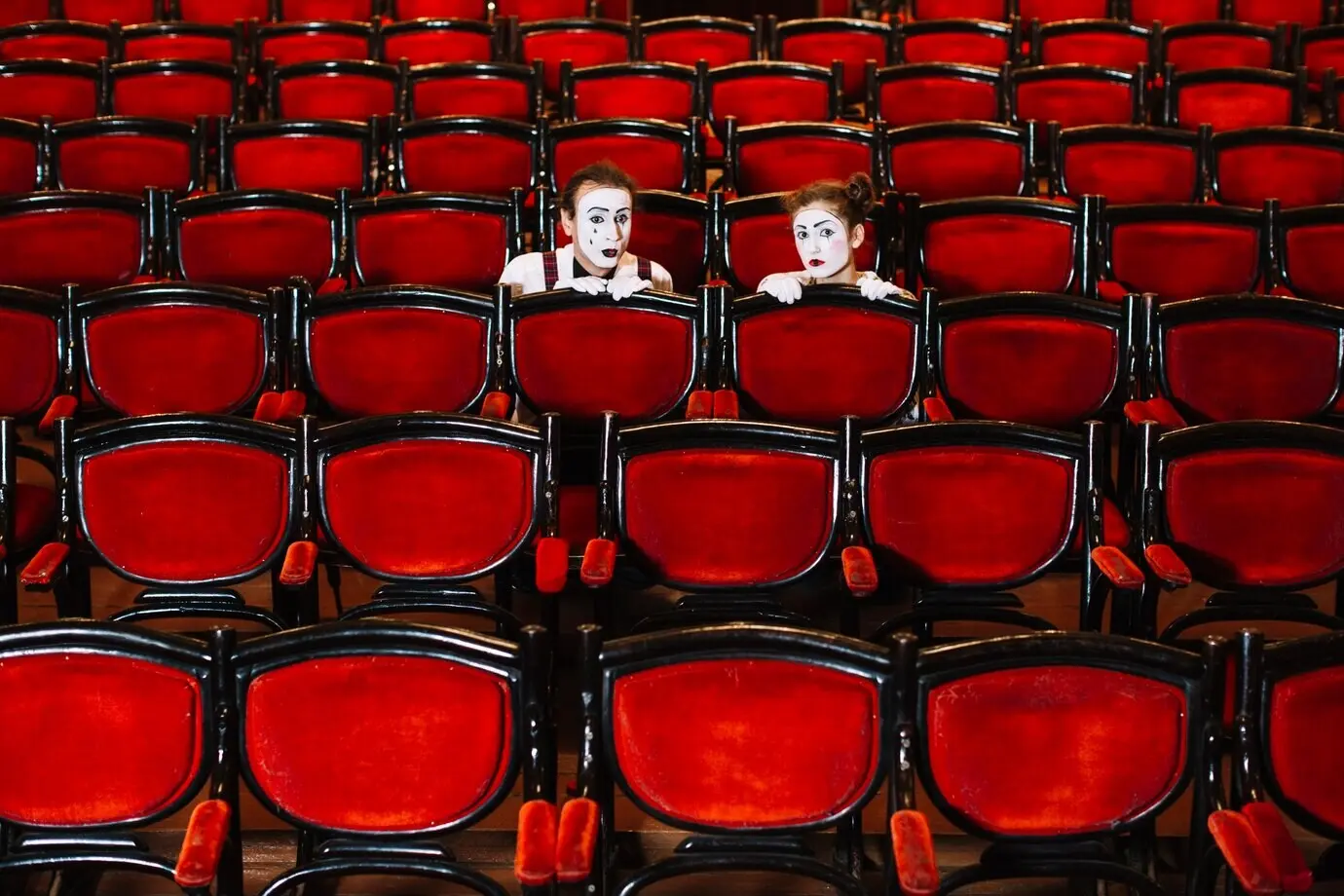 Ein Pantomime und eine Pantomimin verstecken sich hinter der Reihe von Sesseln.